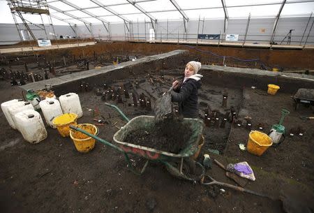 An archaeologist from the University of Cambridge Archaeological Unit, shovels earth while uncovering Bronze Age wooden houses, preserved in silt, from a quarry near Peterborough, Britain, January 12, 2016. REUTERS/Peter Nicholls