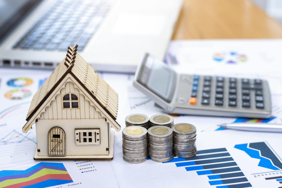 A model of a house next to a stack of coins and a calculator