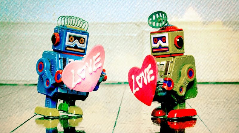 Two robots holding small heart shaped signs saying 'love.'