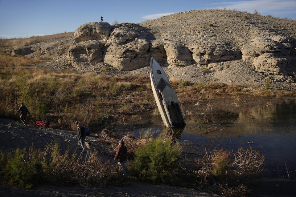 People walk by a formerly sunken boat standing upright into the air with its stern buried in the mud along the shoreline of Lake Mead at the Lake Mead National Recreation Area, Friday, Jan. 27, 2023, near Boulder City, Nev. Six western states that rely on water from the Colorado River have agreed on a plan to dramatically cut their use. California, the state with the largest allocation of water from the river, is the holdout. (AP Photo/John Locher)