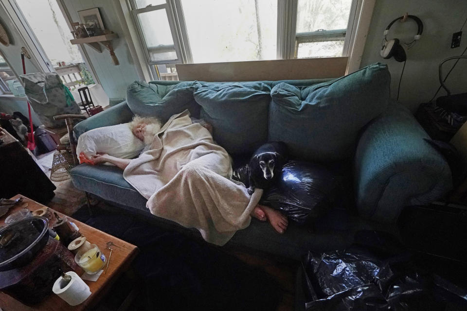 FILE - Dirk Russell, who has medical issues, lies on the sofa in his waterlogged home that flooded in the aftermath of Hurricane Ian on Pine Island, Fla., Saturday, Oct. 1, 2022. The only bridge to the island is heavily damaged so it can only be reached by boat or air. Older people with limited mobility and chronic health conditions were especially vulnerable when Hurricane Ian slammed into Southwest Florida last month. (AP Photo/Gerald Herbert, File)