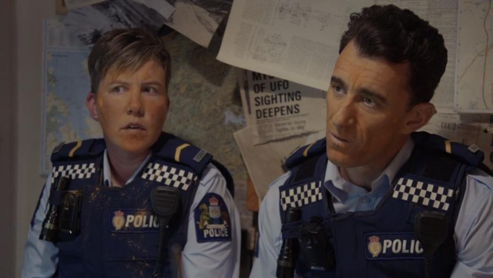 A female and male cop in uniform and vest with orange powder on their faces