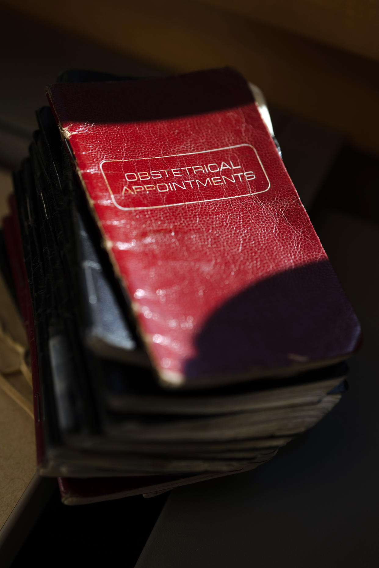 Notebooks where Dr. Bob Ross, 75, has recorded every baby he has delivered are stacked in his office at the hospital in Ortonville, Minn., on Feb. 26, 2024.  Ross has cared for people at both the start and the end of their lives.  (Erin Schaff/The New York Times)