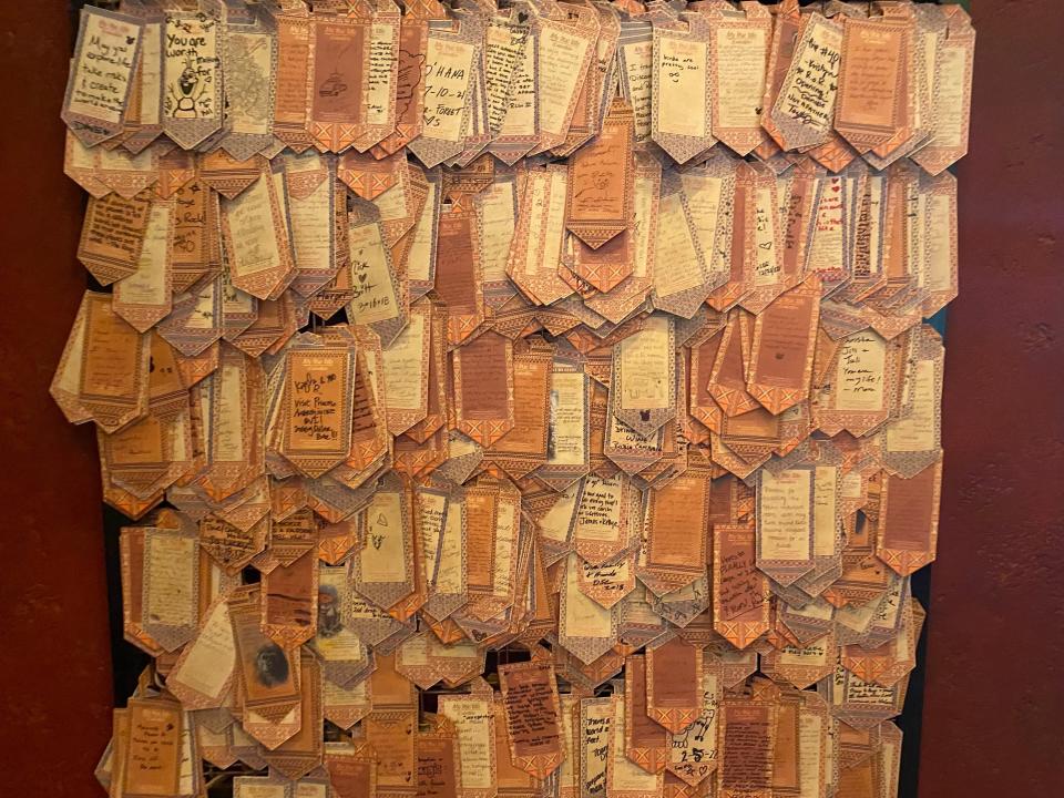 Wall covered in small yellow-orange pieces of paper with people's favorite adventures handwritten on them