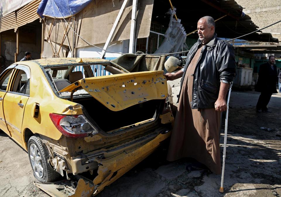 An Iraqi taxi driver inspects his damaged car after a car bomb attack in Baghdad's Karrada neighborhood, Iraq, Thursday, Feb. 6, 2014. Iraqi officials say a string of car bombings has hit commercial areas in Baghdad, killing and wounding scores of people. (AP Photo/Khalid Mohammed)