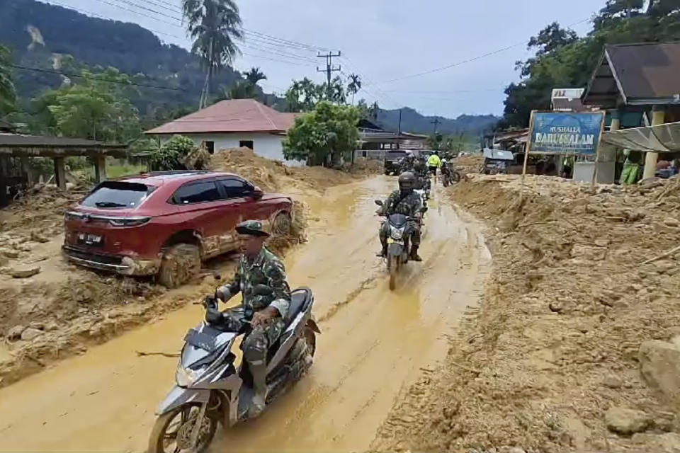 In this image made from video, soldiers ride motor bikes in a village affected by flash flood in Langgai, West Sumatra, Indonesia, Sunday, March 10, 2024. Torrential rains have triggered flash floods and a landslide on Indonesia's Sumatra island leaving a number of people dead and missing, officials said Sunday. (AP Photo)