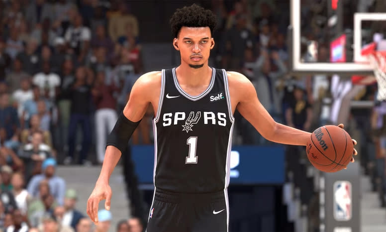 A promotional screenshot from NBA 2K24, showing Spurs rookie Victor Wimpanyama dribbling the ball down the court.  A stadium full of fans visible behind him.