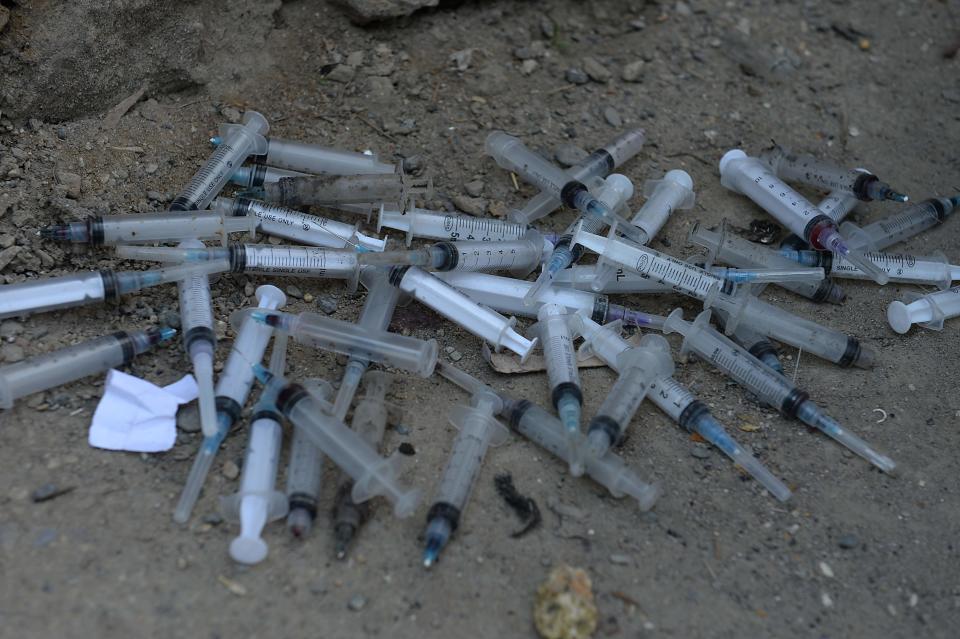 Used syringes and needles are seen under a bridge.