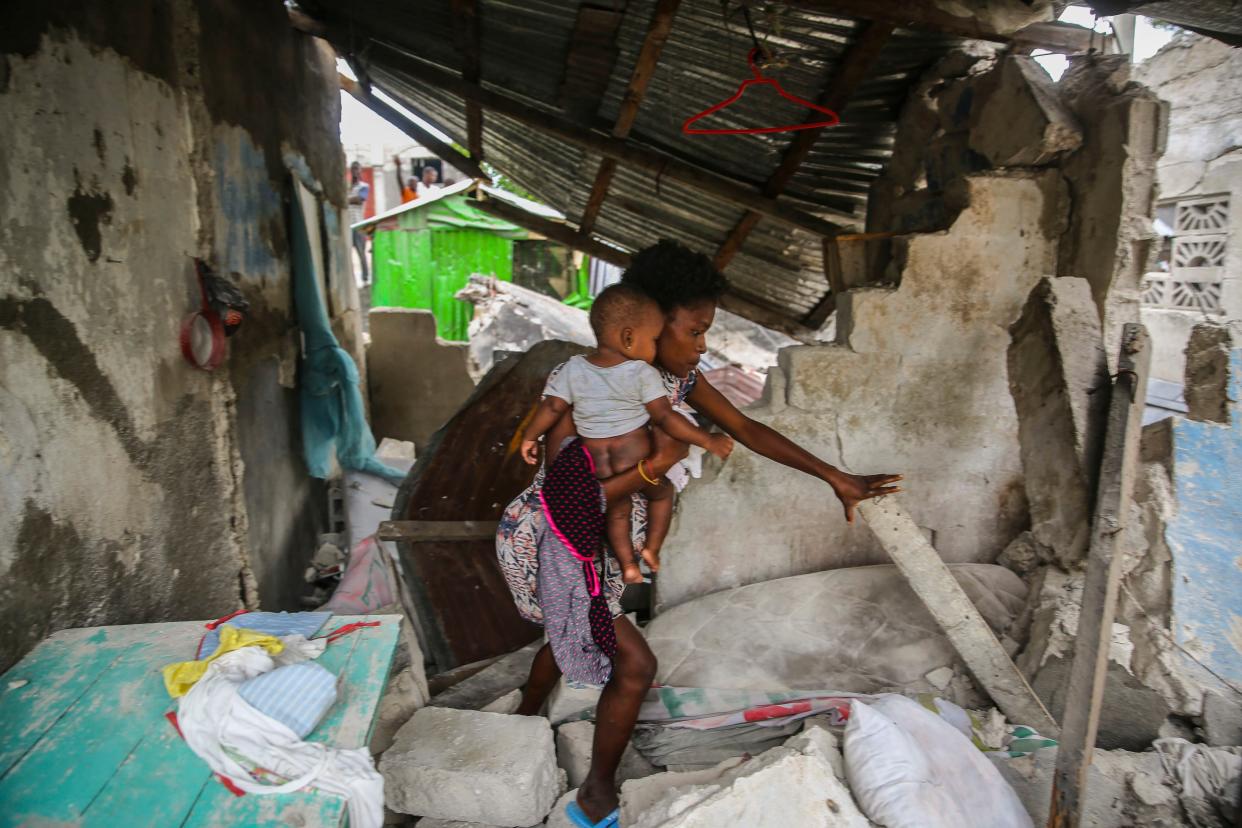 A woman carries her child as she walks in the remains of her home destroyed by Saturday's  7.2 magnitude earthquake in Les Cayes, Haiti, Sunday, Aug. 15, 2021.