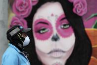 A woman wearing a face mask amid the spread of the new coronavirus walks past a Catrina mural in Bogota, Colombia, Thursday, May 21, 2020. (AP Photo/Fernando Vergara)