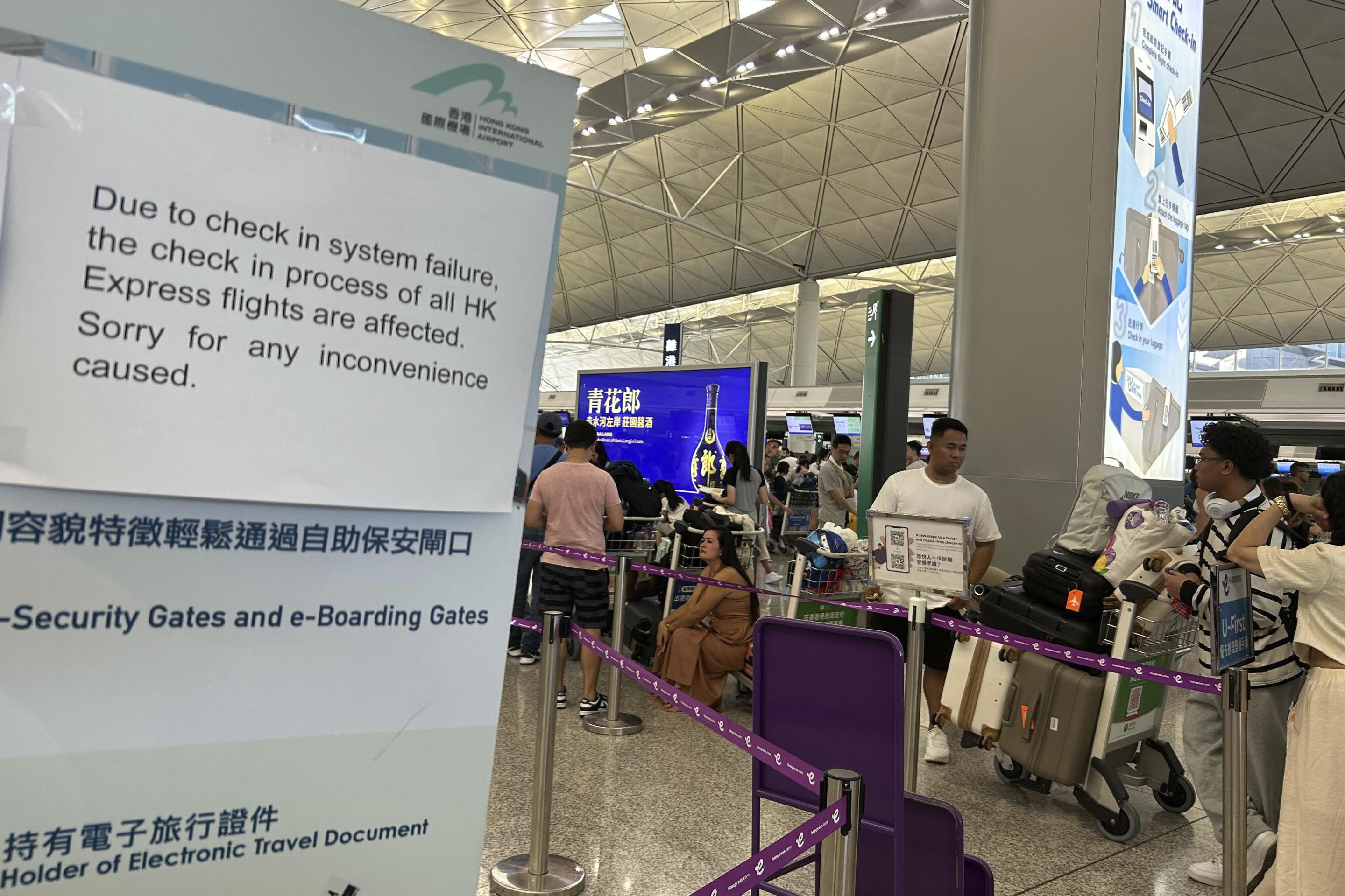 Passengers queue for manual check-in near a sign warning of a check-in system failure at Hong Kong International Airport.