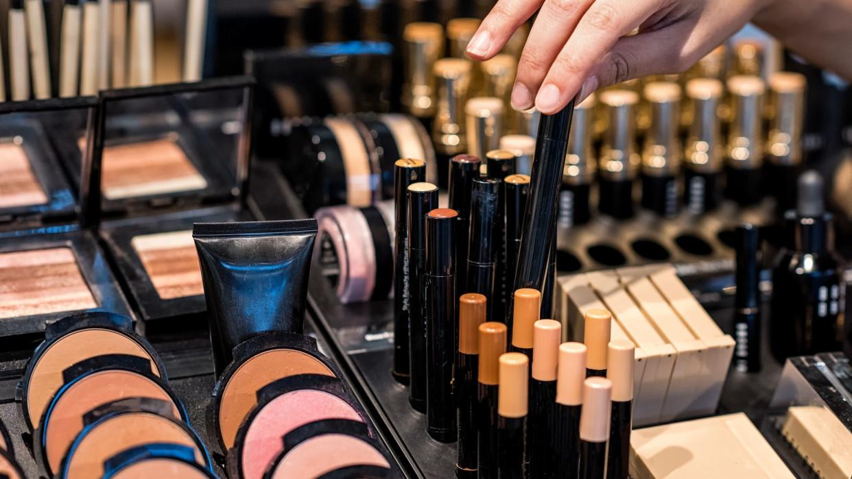 A woman's hand with bracelets chooses from various shades of make-up at a high-end makeup counter.