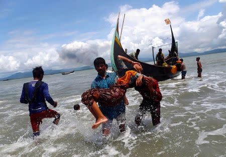 FILE PHOTO: Smoke is seen on Myanmar's side of border as an exhausted Rohingya refugee woman is carried to the shore after crossing the Bangladesh-Myanmar border by boat through the Bay of Bengal, in Shah Porir Dwip, Bangladesh September 11, 2017. REUTERS/Danish Siddiqui/File Photo