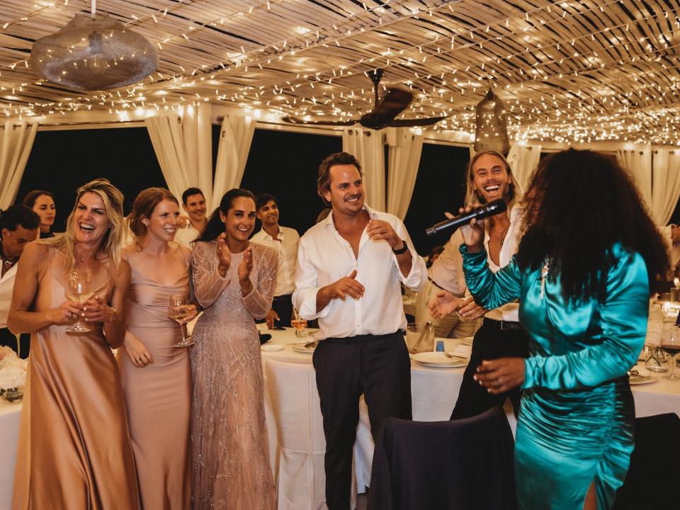 A group of wedding guests dance as a wedding singer in a teal outfit performs.