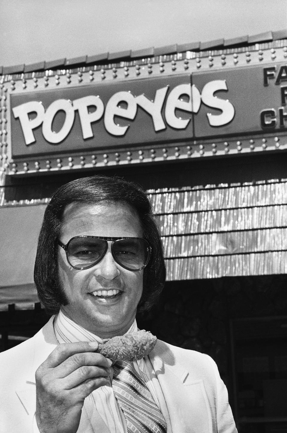 FILE - Popeyes founder Al Copeland holds a piece of his fried chicken outside one of his 34 fast food outlets in New Orleans on June 20, 1979. A new book, “Secrets of a Tastemaker: Al Copeland, The Cookbook," released last month, helped mark the 50th anniversary of Popeyes Famous Fried Chicken. (AP Photo, File)