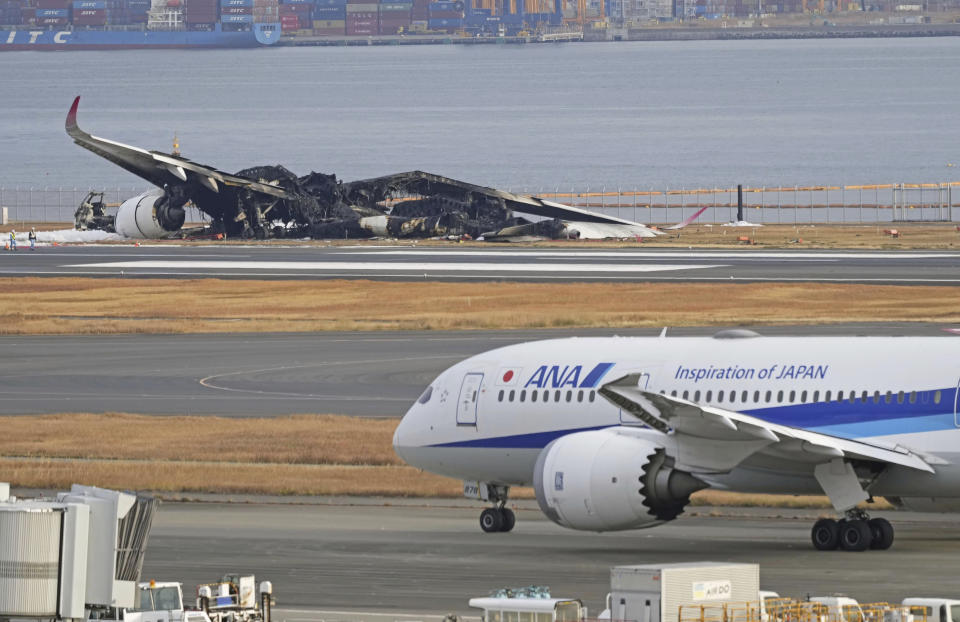The burn-out Japan Airlines plane is seen, at rear, at Haneda airport on Wednesday, Jan. 3, 2024, in Tokyo, Japan. The large passenger plane and a Japanese coast guard aircraft collided on the runway at Tokyo's Haneda Airport on Tuesday and burst into flames, killing several people aboard the coast guard plane, officials said. (Kyodo News via AP)