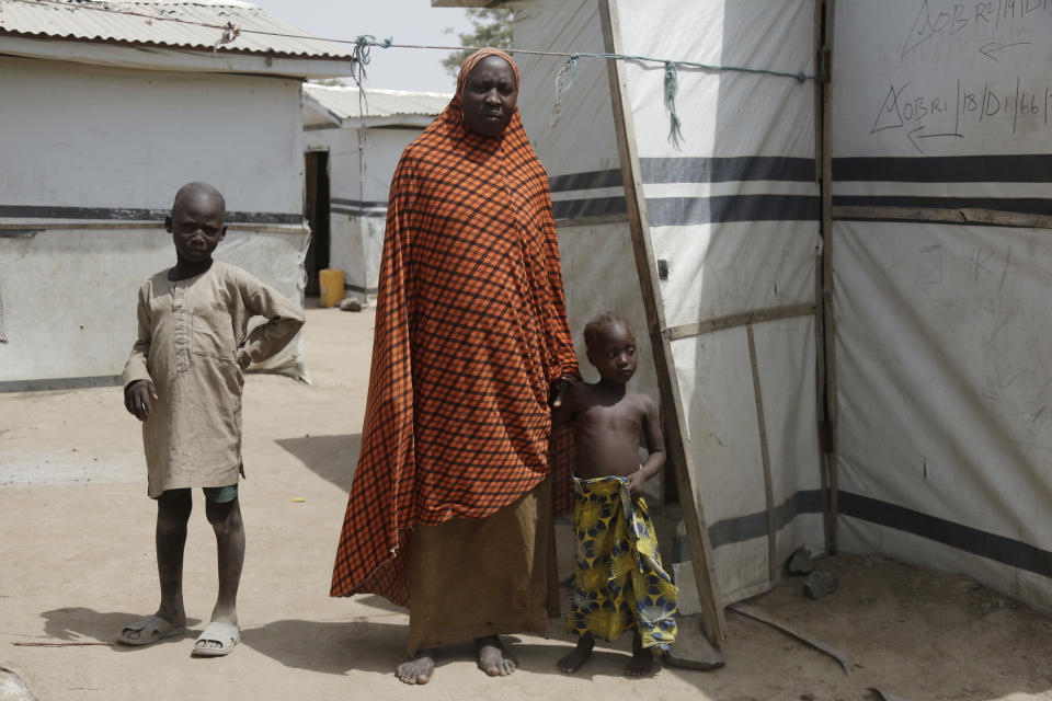 In this photo taken on Monday, Feb. 18, 2019, Fati Umar, a woman displaced by Islamist extremist stands outside her room with her Children at Malkohi camp in Yola, Nigeria. Fati Umar of Gwoza, said she was unable to bury her husband after fleeing a 2014 Boko Haram attack that came while she was cultivating her garden, and for days she hid in the bush with her children. Fati speaks in the makeshift camp for internally displaced people that she shares with hundreds who all have their own story to tell, and who all have more important issues than the upcoming presidential election. (AP Photo/ Sunday Alamba)