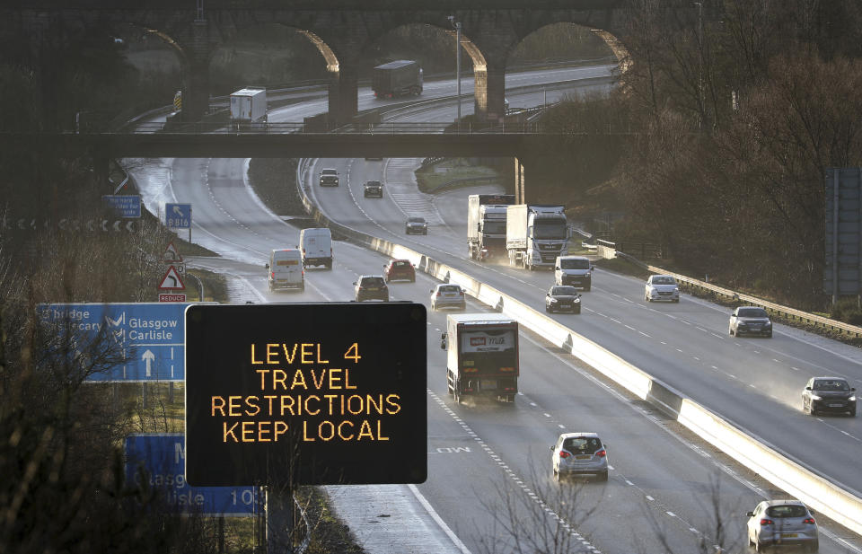 A traffic information board advises drivers to keep their travel to local trips because of coronavirus Level 4 restrictions, as traffic moves along the M80 motorway near Banknock, Scotland, Tuesday Dec. 29, 2020. Scotland has imposed more severe COVID-19 lockdown restrictions for several weeks. (Andrew Milligan/PA via AP)