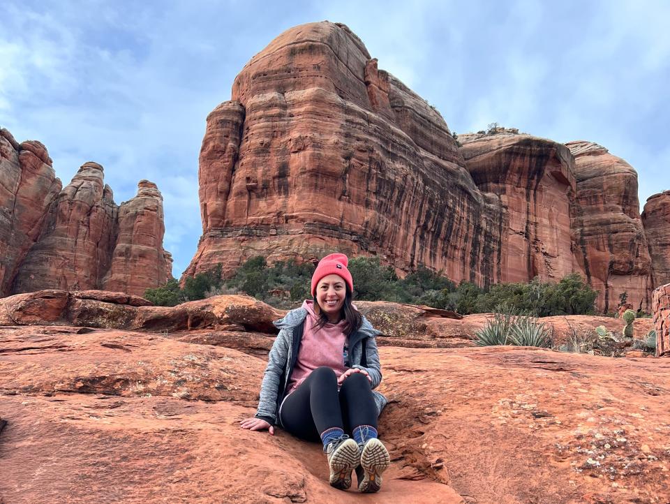 A woman wearing a pink hat sitting on rock in front of sandstone formations.