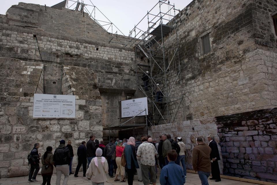 In this Tuesday Dec. 10, 2013 photograph, tourists gather by the entrance to the Church of the Nativity in the West Bank city of Bethlehem. To visitors arriving in Bethlehem for Christmas this year the Nativity Church will look different. Wrapped in scaffolding, the basilica is having a much-needed facelift after 600 years. Last year it has been included in UNESCO's list of endangered World Heritage sites. (AP Photo/Nasser Nasser)