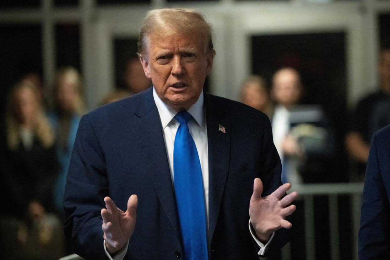 Donald Trump, wearing a navy-blue suit and blue tie, gestures with his hands while speaking.