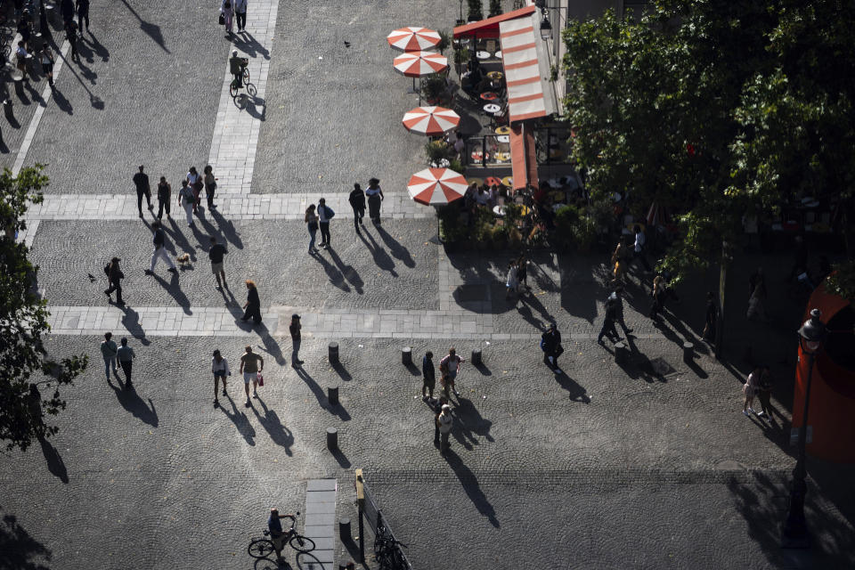 The setting sun casts shadows of pedestrians passing a cafe outside the George Pompidou Beaubourg museum ahead of the 2024 Summer Olympics, Sunday, July 21, 2024, in Paris. (AP Photo/David Goldman)