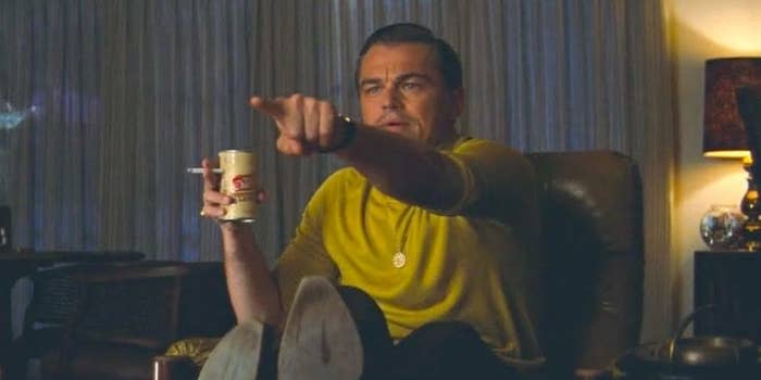 Leonardo DiCaprio, in a yellow shirt, points while holding a drink and a cigarette, in a scene from "Once Upon a Time in Hollywood."