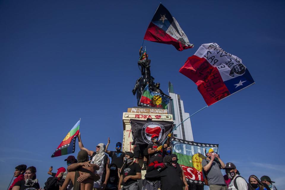 Chileans wave flags while standing on a graffiti-covered national monument.