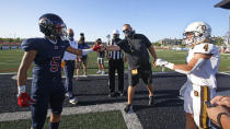 Davis head coach Mitch Arquette, center, fist bumps Herriman's Brock Hollingsworth (5) during the coin toss before the start of a high school football game, on Thursday, Aug. 13, 2020, in Herriman, Utah. Utah is among the states going forward with high school football this fall despite concerns about the ongoing COVID-19 pandemic that led other states and many college football conferences to postpone games in hopes of instead playing in the spring. (AP Photo/Rick Bowmer)