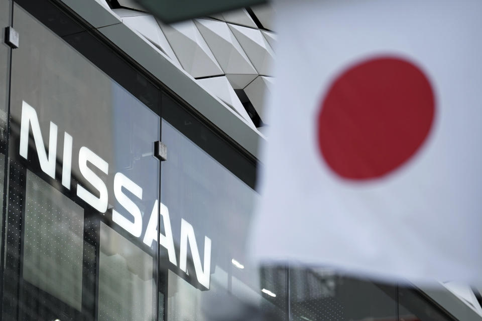 FILE - In this May 10, 2019, file photo, Nissan logo is seen near a Japanese flag at the automaker's showroom in Tokyo. Nissan shareholders unleashed their anger at the Japanese automaker's management Tuesday for crashing stock prices, zero dividends and quarterly losses after the scandal-ridden departure of former Chairman Carlos Ghosn.(AP Photo/Eugene Hoshiko, File)
