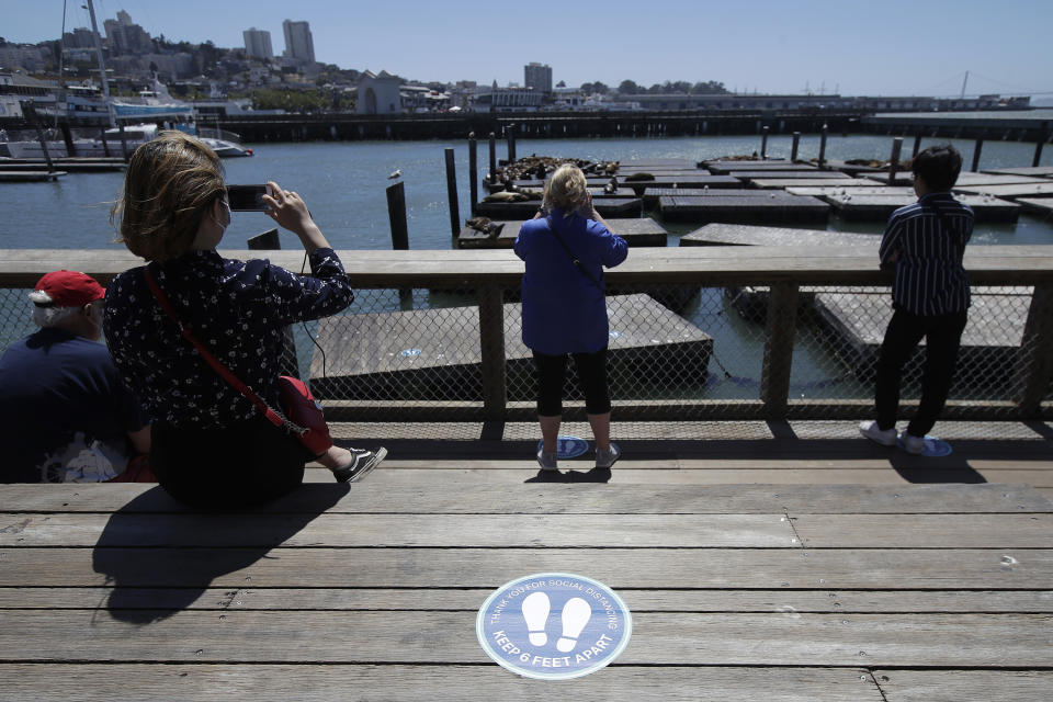 FILE - In this June 18, 2020, file photo, a sign advising visitors to maintain social distance is shown as people watch the sea lions at Pier 39, where some stores, restaurants and attractions have reopened, during the coronavirus outbreak in San Francisco. Health officials in Santa Clara County, California, one of the most aggressive in the nation in shutting down because of the coronavirus are warning of "worrisome" growing infections tied in the San Francisco Bay Area as California reports its highest one-day total infections amid a rise in hospitalizations from the virus. (AP Photo/Jeff Chiu, File)