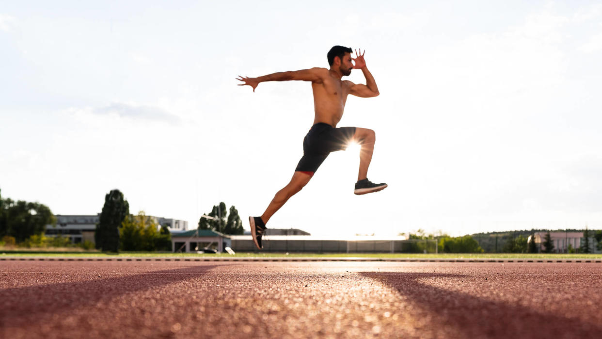 young man exercise jogging and running on athletic track on stadium at sunrise.