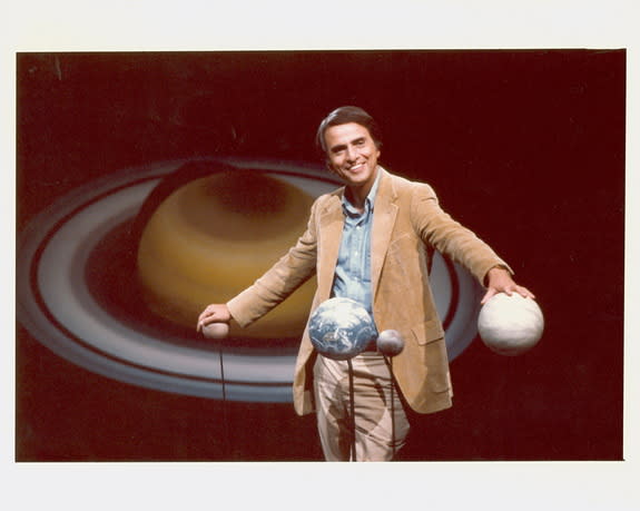 Carl Sagan standing with hands on globes of planets. Undated file photo.