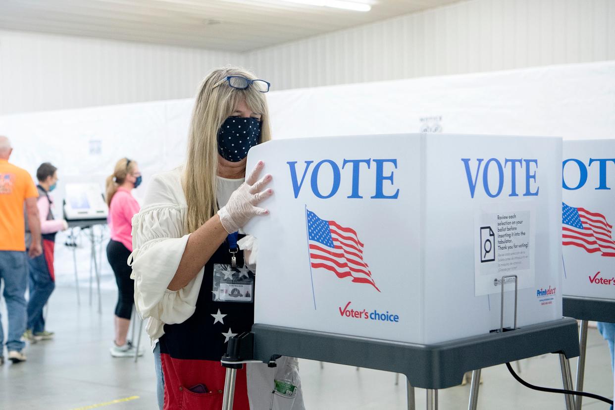 Poll worker Lois Walker cleans a voting computer and privacy shield after a voter cast their ballot during the first day of early voting at the Henderson County Board of Elections Office on Oct. 15, 2020.