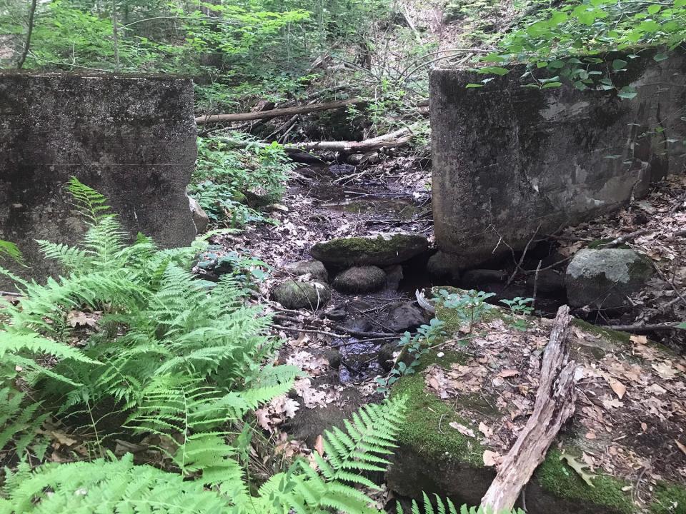 An unnamed brook flows through a gap in an old concrete dam.