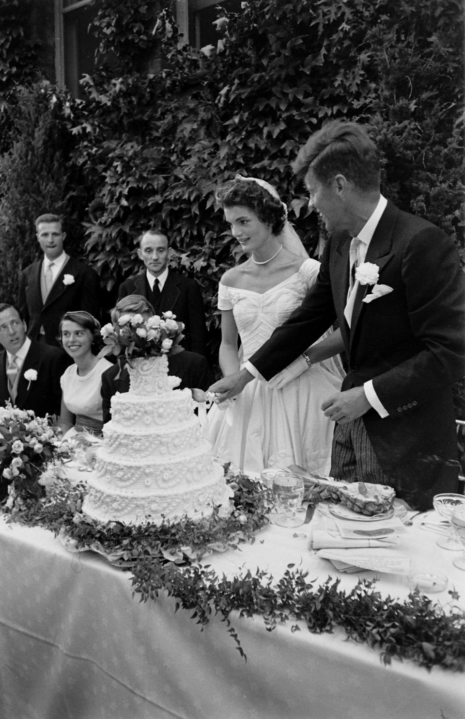 Future US President John F Kennedy (1917 - 1963) and Jacqueline Kennedy (1929 - 1994) (in a Battenburg wedding dress) hold hands as they cut the cake at their wedding reception, Newport, Rhode Island, September 12, 1953. (Photo by Lisa Larsen/Time & Life Pictures/Getty Images)