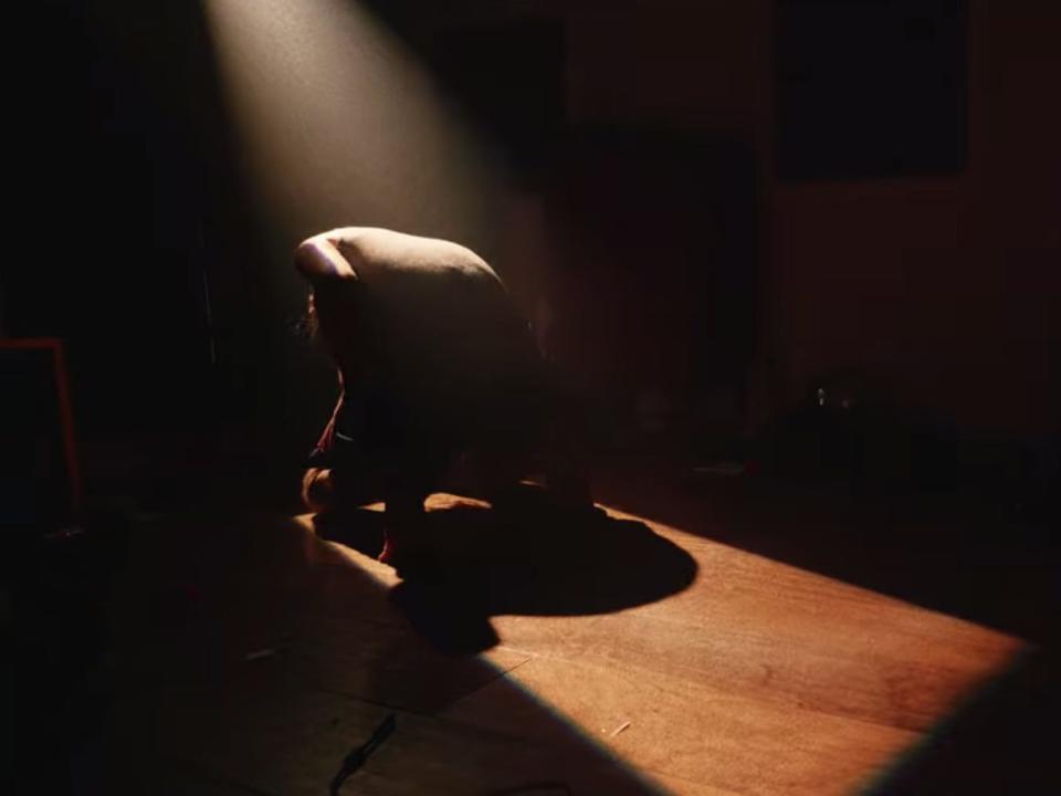 Bo Burnham kneeling down in a beam of light during the music video for "Problematic."