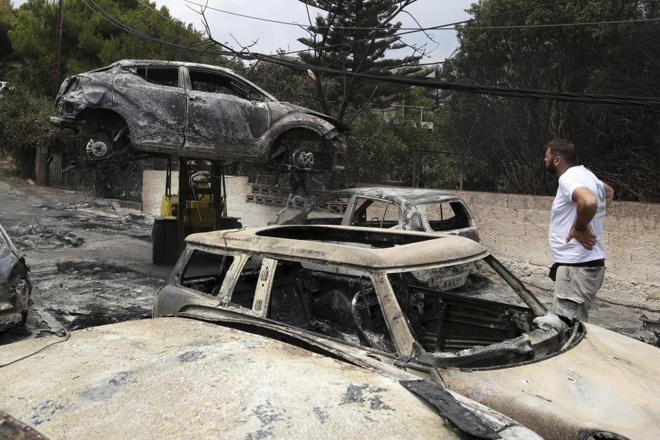 A crane removes a burned car from the road in Mati, east of Athens, Tuesday, July 24, 2018. Wildfires raged through seaside resorts near the Greek capital, torching homes, cars and forests and killing at least 74 people, authorities said Tuesday. (AP Photo/Thanassis Stavrakis)