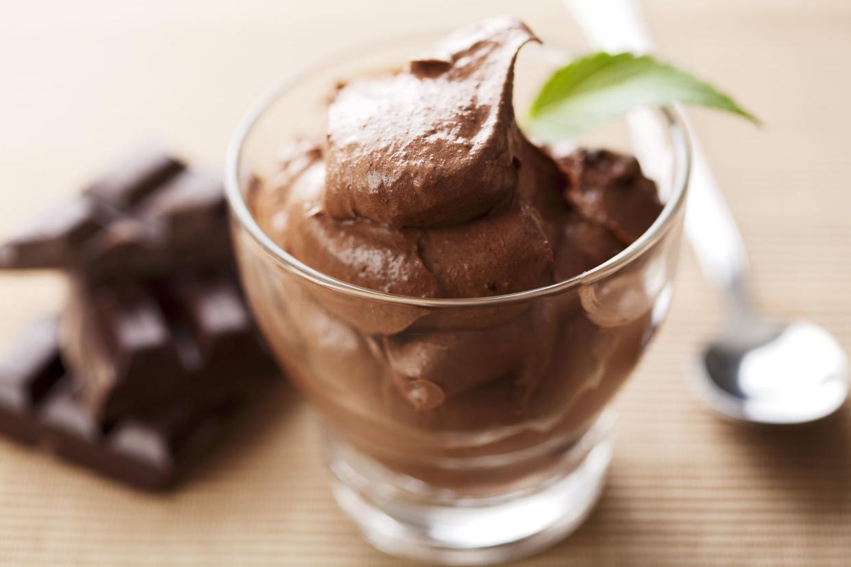 Closeup of low carb diabetic chocolate mousse in a glass dessert bowl with a blurred background of chocolate pieces and a dessert spoon on a table