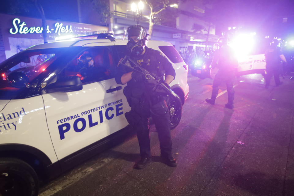 A federal officer stands by a police vehicle during a Black Lives Matter protest early Saturday, July 25, 2020, in Portland, Ore. On the streets of Portland, a strange armed conflict unfolds night after night. It is raw, frightening and painful on both sides of an iron fence separating the protesters on the outside and federal agents guarding a courthouse inside. This weekend, journalists for The Associated Press spent the weekend both outside, with the protesters, and inside the courthouse, with the federal agents, documenting the fight that has become an unlikely centerpiece of the protest movement gripping America. (AP Photo/Marcio Jose Sanchez)