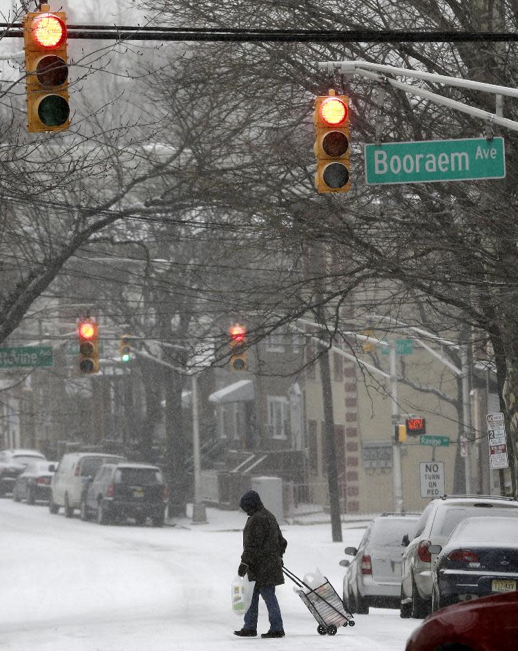 A woman pulls a cart as she walks across the street covered with snow, Tuesday, Jan. 21, 2014, in Jersey City, N.J. A storm is expected to hit the northern New Jersey region throughout the day. Because of hazardous driving conditions New Jersey Gov. Chris Christie's inauguration party at Ellis Island was cancelled. (AP Photo/Julio Cortez)