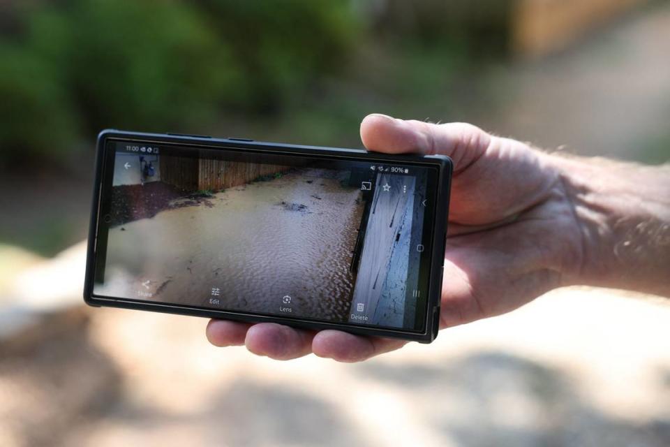 Andrew Farnie shows a photo on his cell phone with ankle-deep water in his driveway due to stormwater runoff from new housing construction on his street.