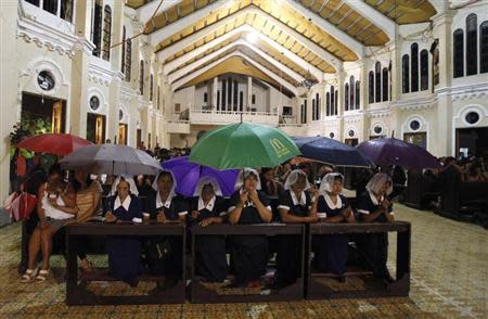Devotees shelter themselves from the rain during a mass at dawn inside a metropolitan Cathedral damaged by super typhoon Haiyan last month, in Palo, Leyte December 24, 2013. REUTERS/Romeo Ranoco
