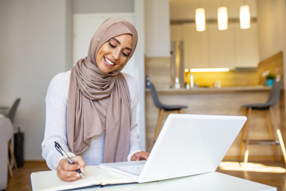 Attractive female Arabic working on laptop computer and paperwork's on desk. Arabian Businesswoman working at home. Dedication and technology. Essential for getting her tasks done