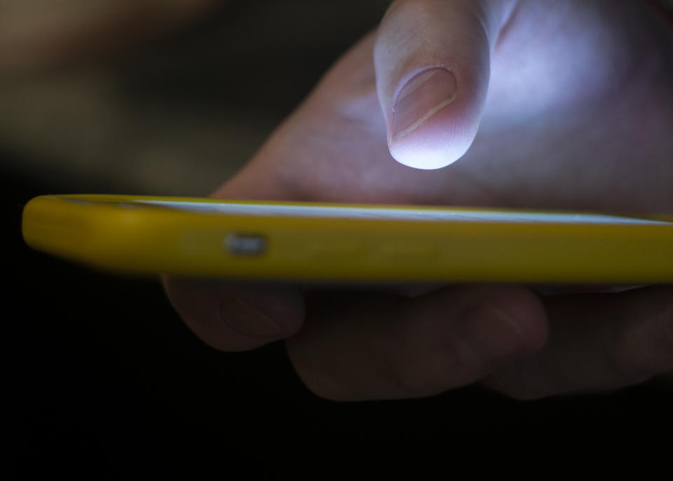 A thumb hovers over a cellphone in the dark.