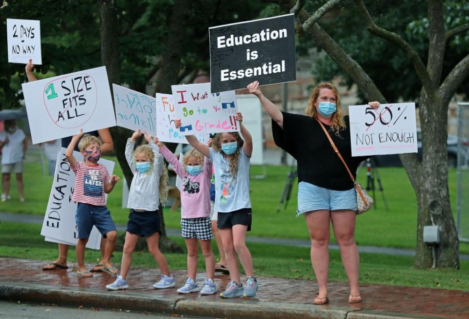 Young elementary school students and their parents attempt to get the attention of passing motorists on Church Street in Winchester, MA on July 30, 2020. A group of Winchester parents hold an event on the town common, voicing their concerns about younger students being able to learn remotely and advocating for the full return of them to classrooms.