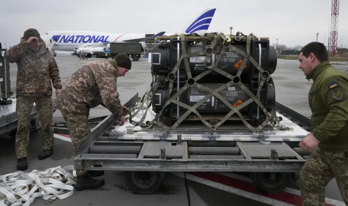 Servicemen unpack military equipment on a tarmac near an airplane with National printed on the side.