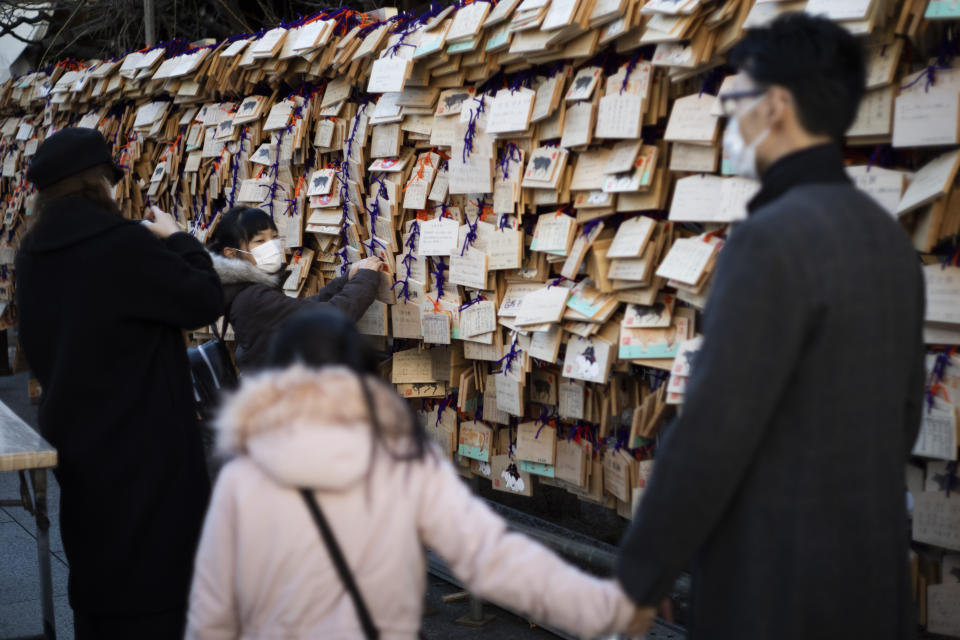 A girl with her family members hangs her "ema" board with her wish written on it in Yushima Tenmangu shrine in Tokyo on New Year's Day, Friday, Jan. 1, 2021. (AP Photo/Hiro Komae)