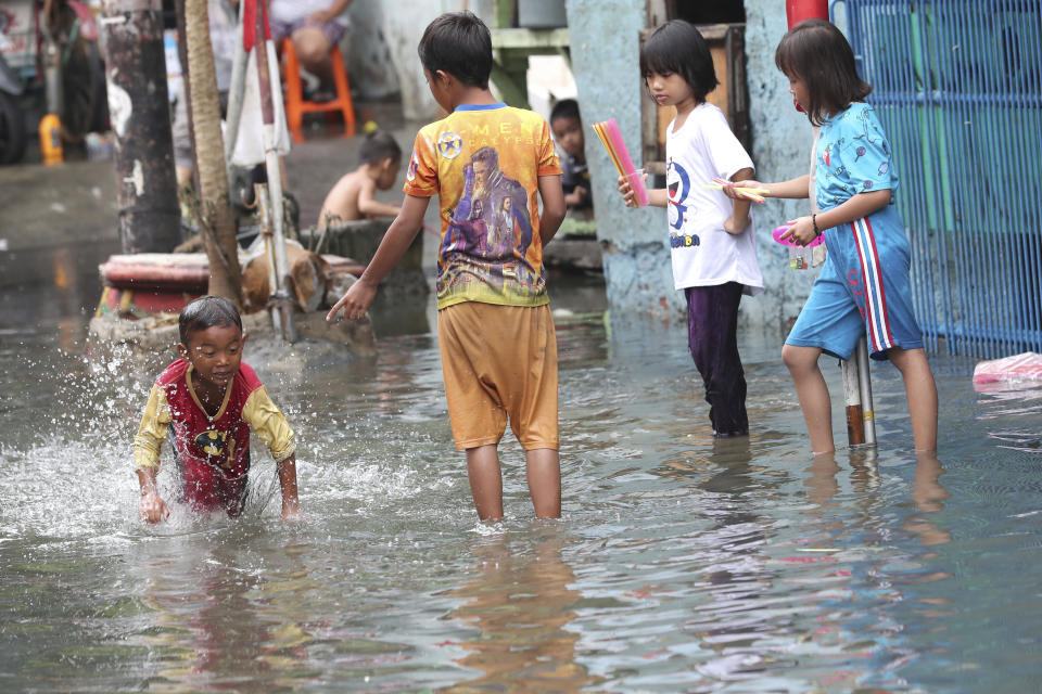 Children play on a flooded street in Jakarta, Indonesia, Sunday, Jan. 5, 2020. Landslides and floods triggered by torrential downpours have left dozens of people dead in and around Indonesia's capital, as rescuers struggled to search for people apparently buried under tons of mud, officials said Saturday. (AP Photo/Tatan Syuflana)