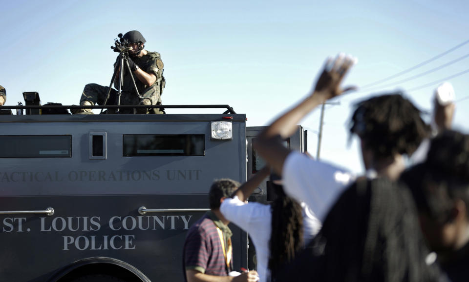 FILE - In this Wednesday, Aug. 13, 2014 file photo, a member of the St. Louis County Police Department points his weapon in the direction of a group of protesters in Ferguson, Mo. On Saturday, Aug. 9, 2014, a white police officer fatally shot Michael Brown, a Black teenager, in the St. Louis suburb. (AP Photo/Jeff Roberson, File)